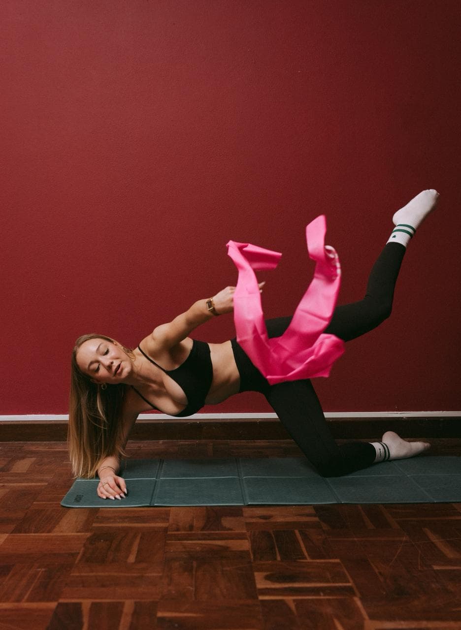A side plank on the mat, one leg lifted against a pink resistance band.